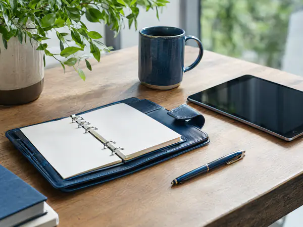 Desk with a planner, pen, tablet and mug set up for a client meeting