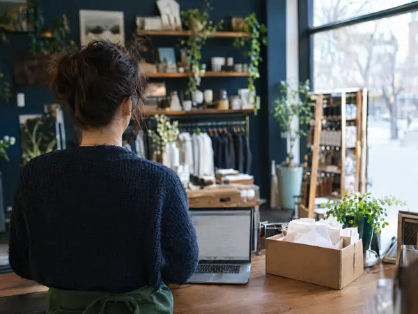 Small-business owner at a shop counter with a laptop and a box of receipts to organize