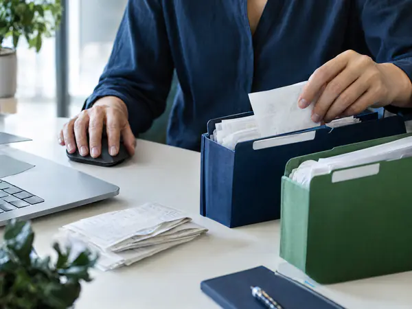Hands sorting receipts into labeled folders next to a computer mouse